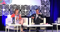 Two people sitting on stage in a panel discussion at a conference.